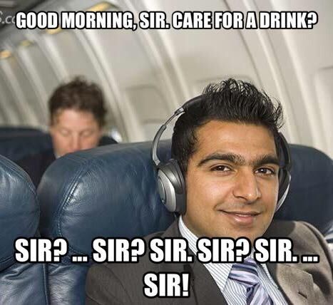 man in headphones ignoring flight attendant on a plane.